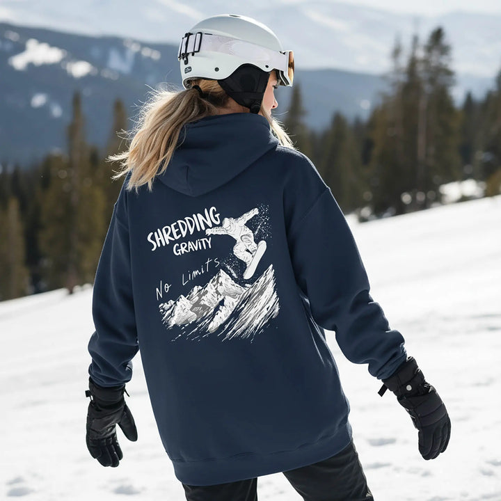 Person wearing a navy hoodie with 'Shredding Gravity No Limits' graphic in a snowy mountain setting